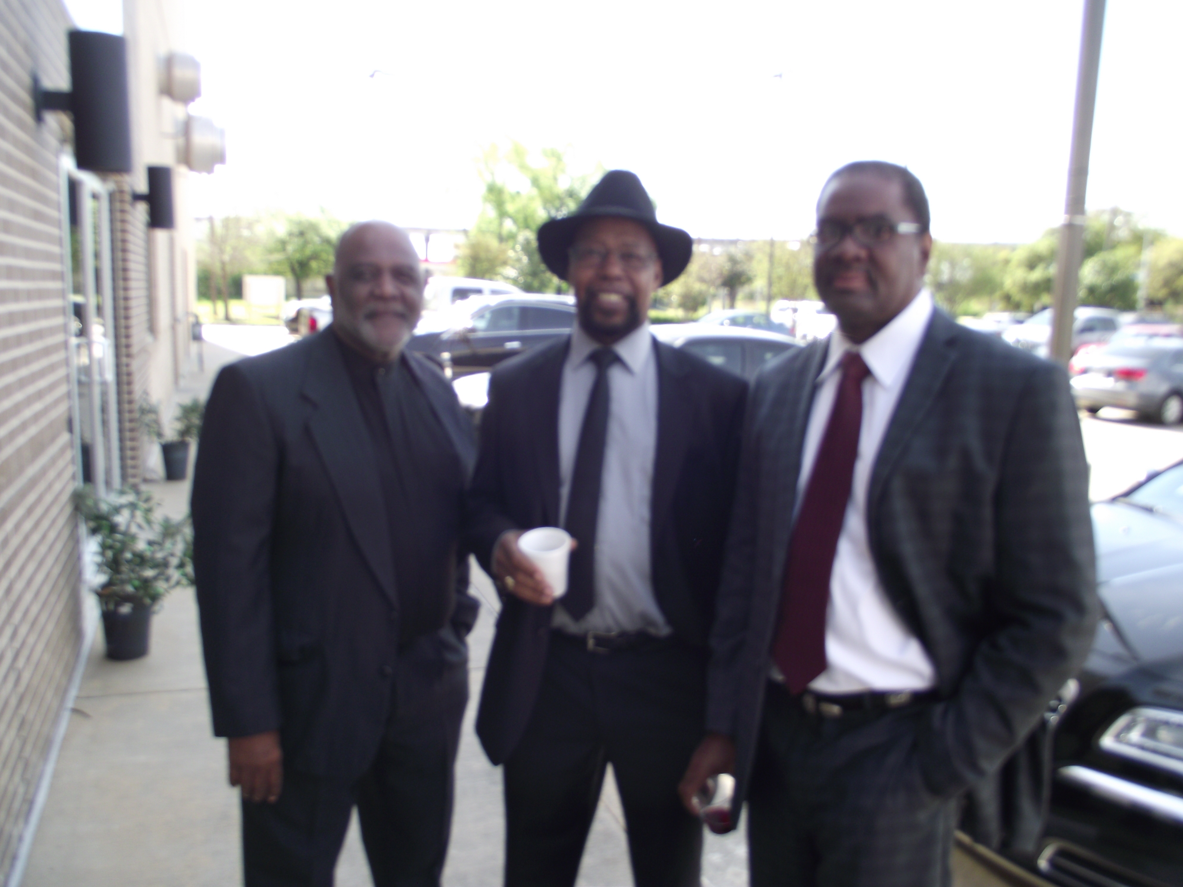 Three men in suits and hats are standing outside.