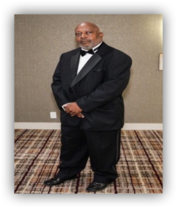 Man in tuxedo standing on patterned carpet.