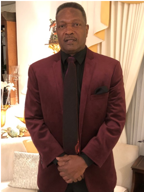 Man in burgundy suit, standing indoors.