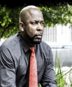 Man in shirt and tie outdoors, thoughtful expression.