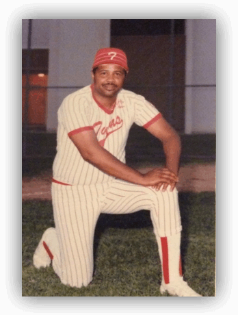 Baseball player kneeling on grass in uniform.