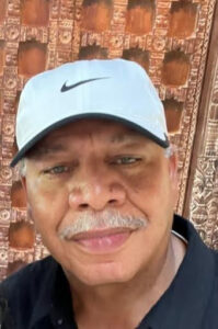 Man wearing white cap, wooden carved backdrop.