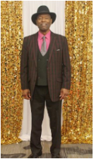 Man in suit with gold curtain backdrop.