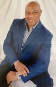 Man in blue suit, smiling, seated pose.